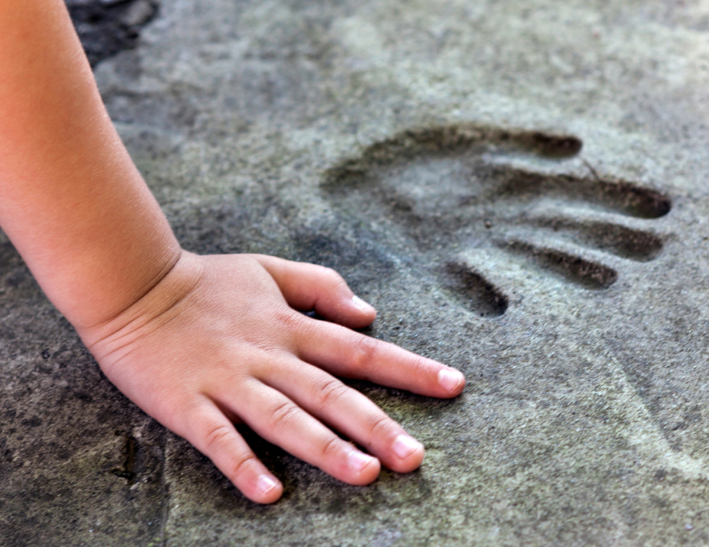 a child pressing thier hand into handprints on cement